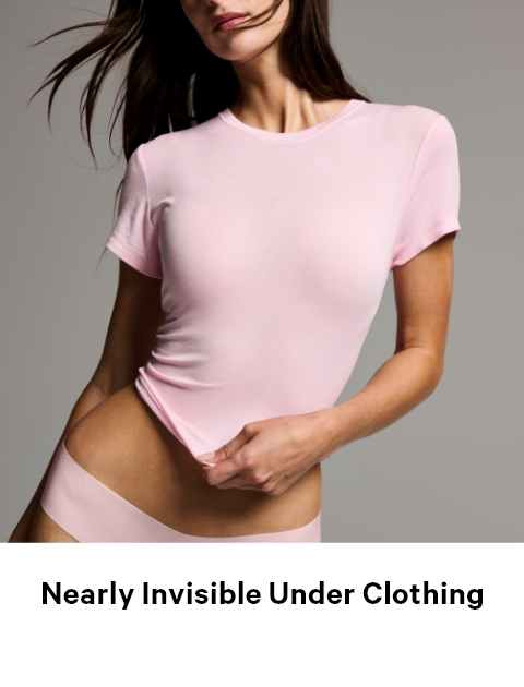 Woman posing in a baby pink t-shirt and panties on a gray background.