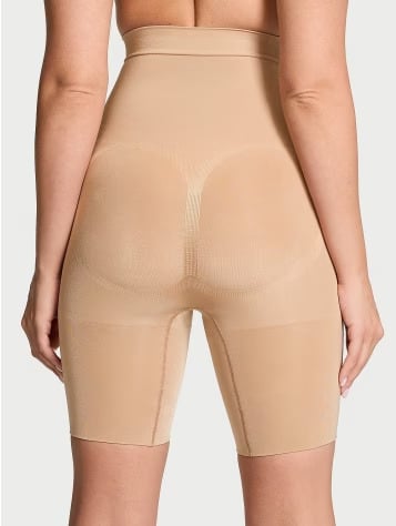 Back view of a women wearing Victoria's Secret beige lower body shapewear on a light grey background