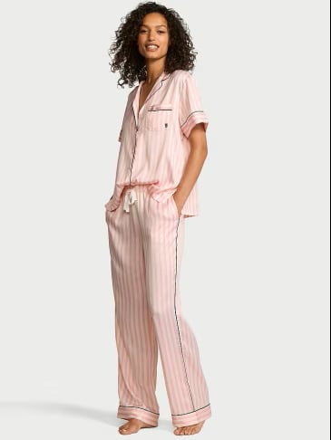 Full body view of woman wearing Victoria's Secret signature stripes pijama set on a light grey background.