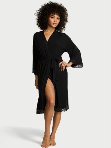 Full body view of woman wearing Victoria's Secret black Modal Lace-Trim Robe on a light grey background.